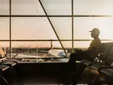Mężczyzna w czapce siedzi na lotnisku AMS, czekając na samolot w blasku zachodzącego słońca.