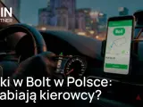 Kierowca w rękawiczkach trzyma kierownicę, na desce rozdzielczej widoczny telefon z aplikacją Bolt. Sprawdź, ile zarobisz za km w Bolt.