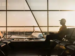 Mężczyzna w czapce siedzi na lotnisku AMS, czekając na samolot w blasku zachodzącego słońca.