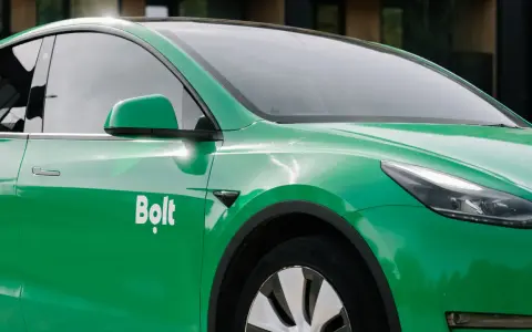 Zielone auto z oklejeniem Bolt. Widoczna część drzwi, lusterko i fragment maski.