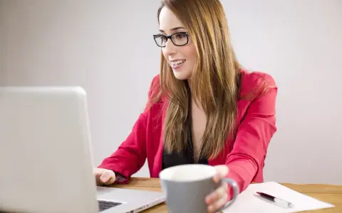 Uśmiechnięta kobieta w okularach pracuje przy laptopie, zastanawiając się, czy można dokupić AC do ubezpieczenia.
