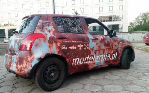 Samochód z okleiną imitującą rdzę, z napisem "modelarnia.pl" i ikonami modeli. Reklama na samochodzie zarobek.