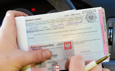 Dłoń trzyma mandat karny i dowód osobisty.