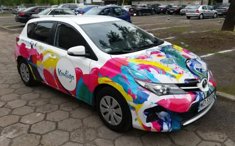 Kolorowe oklejone samochody z logo "Koutigo" na parkingu.