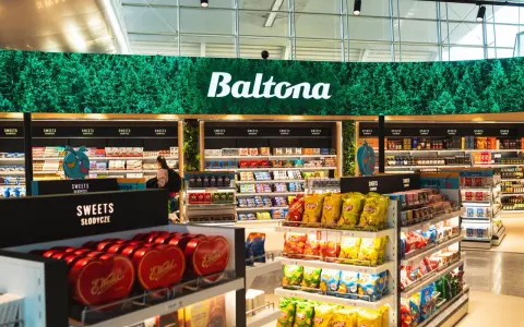 Sklep Baltona na lotnisku Poznań oferuje szeroki wybór słodyczy i alkoholi. Widać tu półki pełne czekolad, chipsów i innych przekąsek.