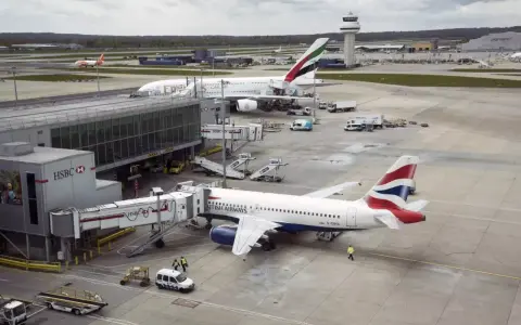 Samoloty British Airways i Emirates czekają na pasażerów na lotnisku Gatwick. W tle widać wieżę kontroli lotów.