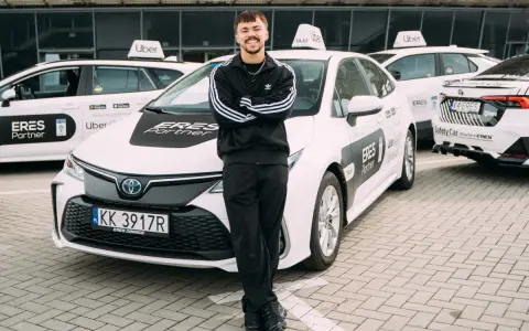 Młody mężczyzna w dresie stoi przed białymi samochodami Uber z napisem "ERES Partner". To jego praca prywatny kierowca.