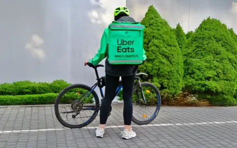 Dostawca Uber Eats w zielonej kurtce i kasku stoi obok roweru.