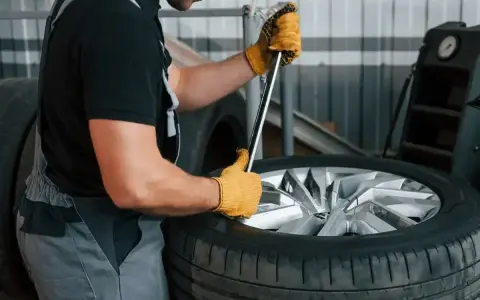Mechanik w żółtych rękawiczkach używa klucza do odkręcania śrub, pokazując, jak ściągnąć oponę z felgi.