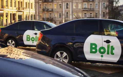 Ciemne samochody z logo Bolt, gotowe do pracy taxi bez licencji, stoją na ulicy.