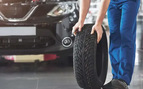 Mechanik pokazuje, jak założyć opony w dobrym kierunku. Widać bieżnik i czarne auto.