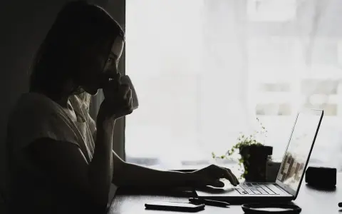 Kobieta pije kawę, pracując na laptopie. Może właśnie przegląda umowa zlecenie kierowca, planując swoją karierę.