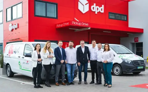 Zespół DPD pozuje przed budynkiem z logo firmy i elektrycznym dpd bus.