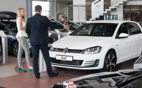 Sprzedawca prezentuje biały samochód flotowy Volkswagen Golf klientce w salonie samochodowym.