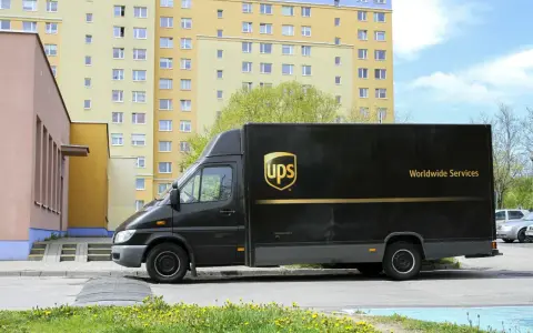 Czarny van UPS z napisem "Worldwide Services" na tle bloku mieszkalnego. Zastanawiasz się, ile zarabia kurier UPS?