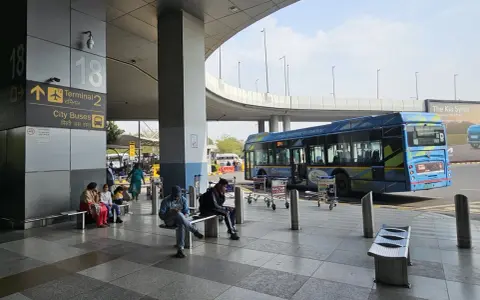 Oczekujący na autobusy na lotnisku Delhi. W tle niebieski autobus elektryczny.