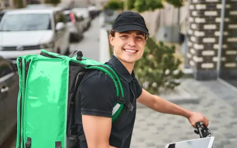 Uśmiechnięty kurier Bolt Food z zieloną torbą na plecach, gotowy do pracy i dobrych zarobków.