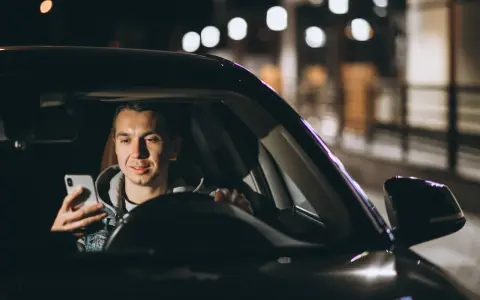 Mężczyzna w samochodzie Uber Black sprawdza telefon, planując trasę i licząc na dobre uber black zarobki.
