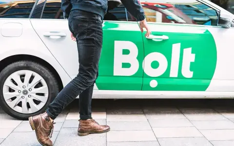 Chcesz wiedzieć, jak zostać kierowcą Bolta? Mężczyzna otwiera drzwi białego samochodu z zielonym logo Bolt.