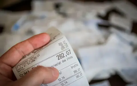 Dłoń trzyma paragon z widoczną kwotą 282,07 zł.