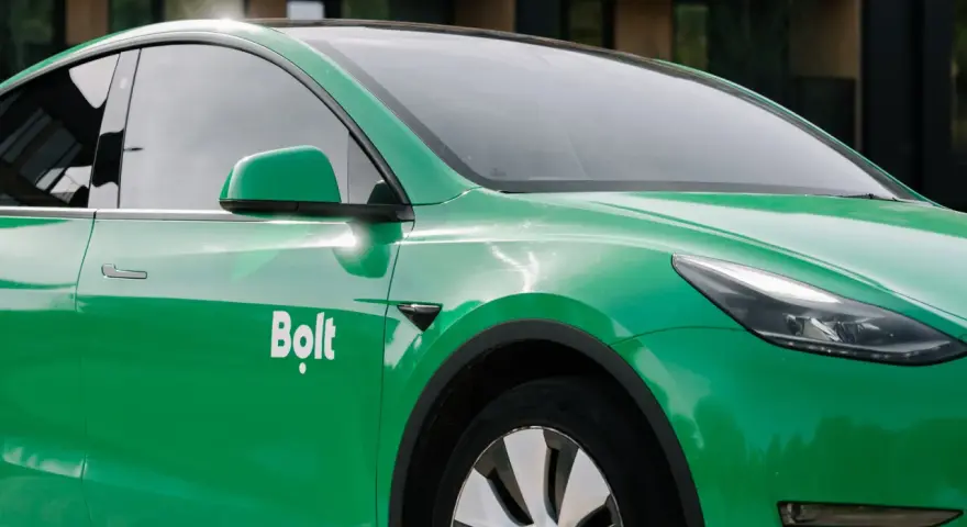 Zielone auto z oklejeniem Bolt. Widoczna część drzwi, lusterko i fragment maski.