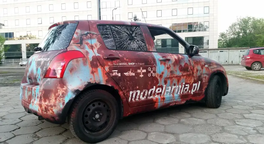 Samochód z okleiną imitującą rdzę, z napisem "modelarnia.pl" i ikonami modeli. Reklama na samochodzie zarobek.