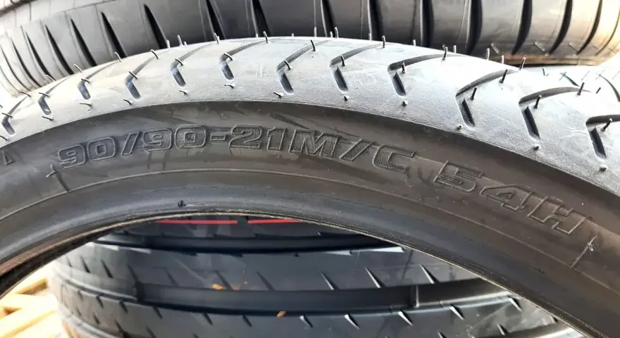 Zbliżenie na przekrój opony motocyklowej z widocznym rozmiarem 90/90-21M/C 54H.