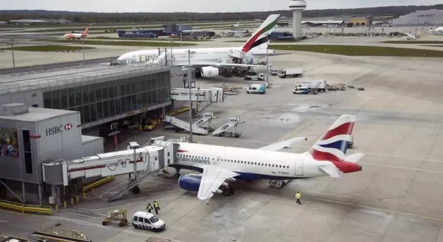 Samoloty British Airways i Emirates czekają na pasażerów na lotnisku Gatwick. W tle widać wieżę kontroli lotów.