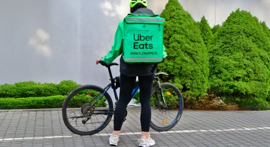 Dostawca Uber Eats w zielonej kurtce i kasku stoi obok roweru.