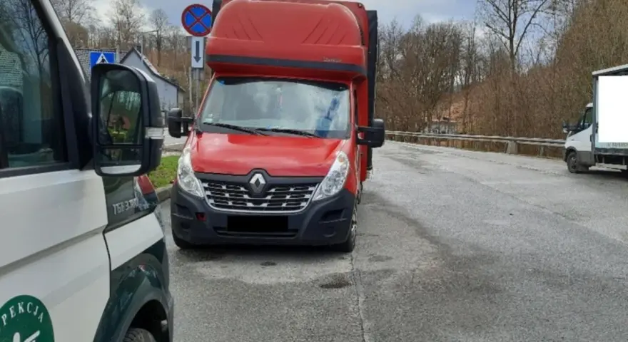 Czerwony bus Renault na drodze, obok pojazd inspekcji. Może to być związane z wnioskiem o wypis z licencji transportowej.