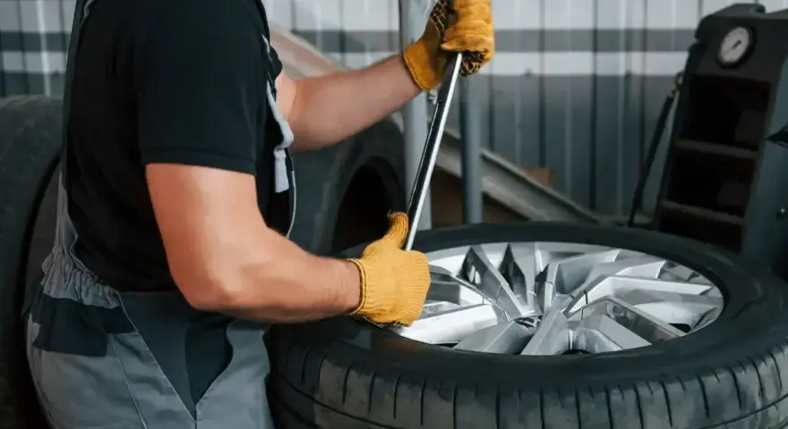 Mechanik w żółtych rękawiczkach używa klucza do odkręcania śrub, pokazując, jak ściągnąć oponę z felgi.