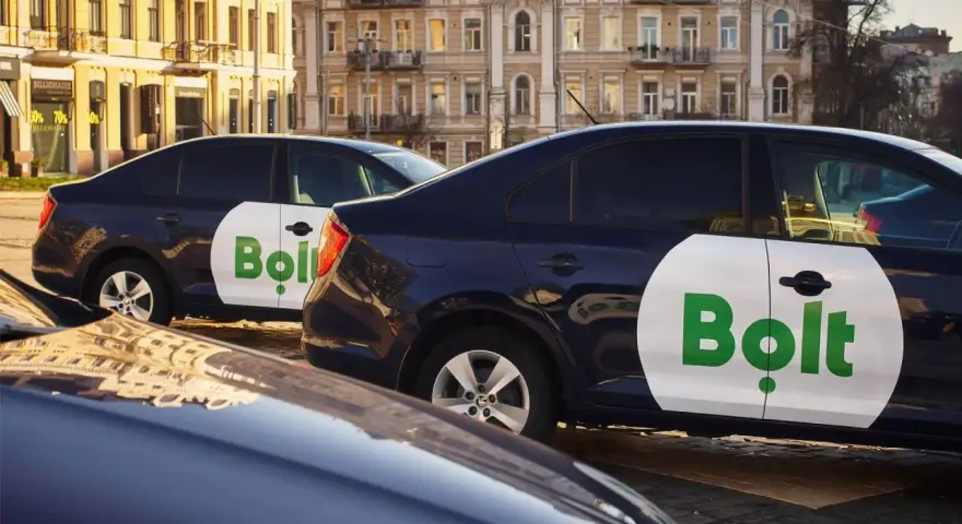 Ciemne samochody z logo Bolt, gotowe do pracy taxi bez licencji, stoją na ulicy.