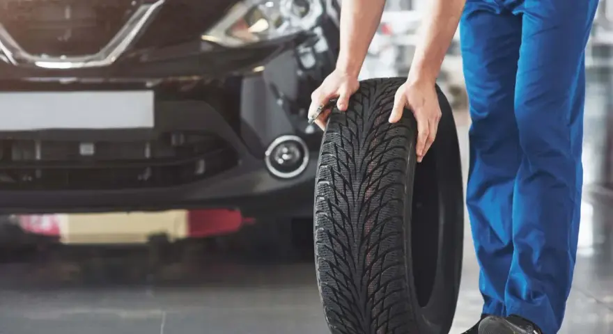 Mechanik pokazuje, jak założyć opony w dobrym kierunku. Widać bieżnik i czarne auto.