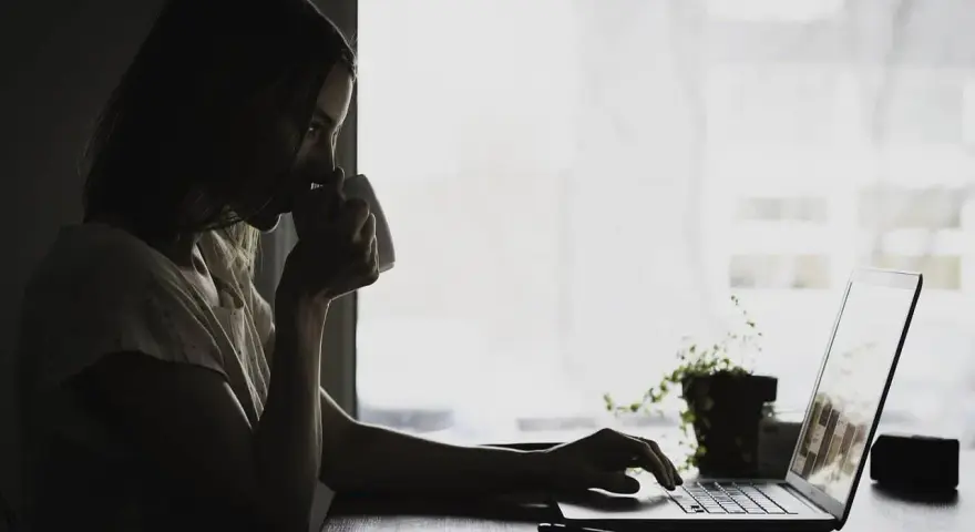 Kobieta pije kawę, pracując na laptopie. Może właśnie przegląda umowa zlecenie kierowca, planując swoją karierę.