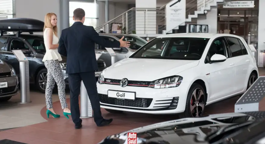 Sprzedawca prezentuje biały samochód flotowy Volkswagen Golf klientce w salonie samochodowym.