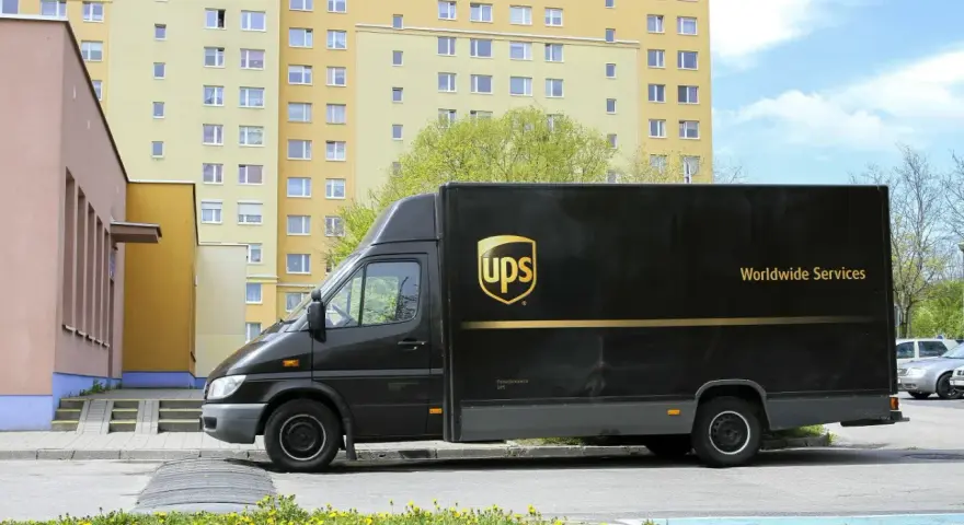 Czarny van UPS z napisem "Worldwide Services" na tle bloku mieszkalnego. Zastanawiasz się, ile zarabia kurier UPS?