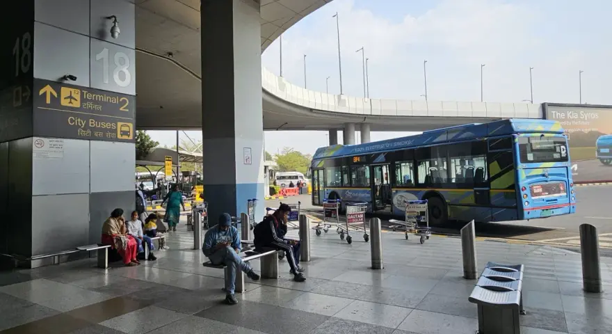 Oczekujący na autobusy na lotnisku Delhi. W tle niebieski autobus elektryczny.