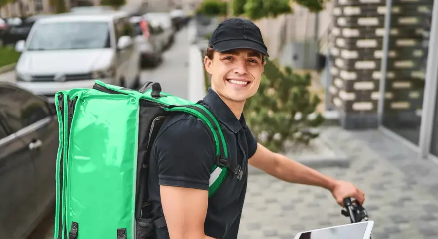 Uśmiechnięty kurier Bolt Food z zieloną torbą na plecach, gotowy do pracy i dobrych zarobków.
