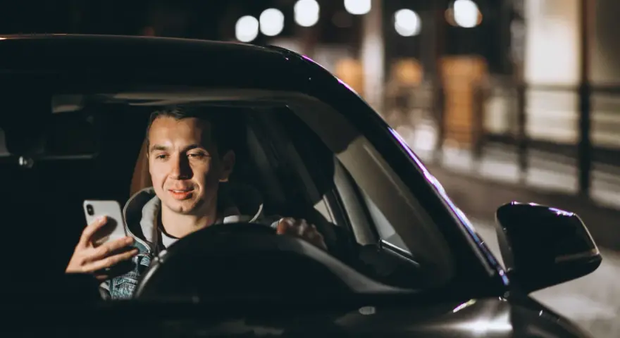Mężczyzna w samochodzie Uber Black sprawdza telefon, planując trasę i licząc na dobre uber black zarobki.