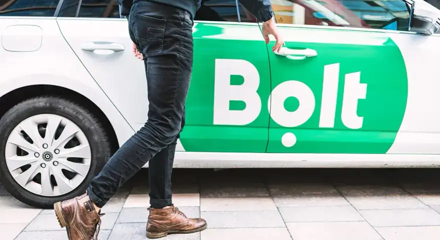 Chcesz wiedzieć, jak zostać kierowcą Bolta? Mężczyzna otwiera drzwi białego samochodu z zielonym logo Bolt.