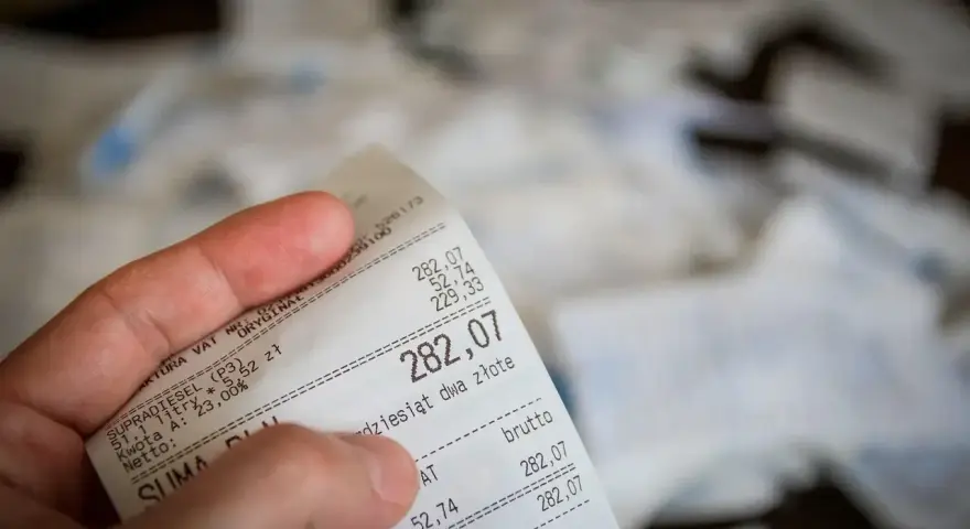 Dłoń trzyma paragon z widoczną kwotą 282,07 zł.